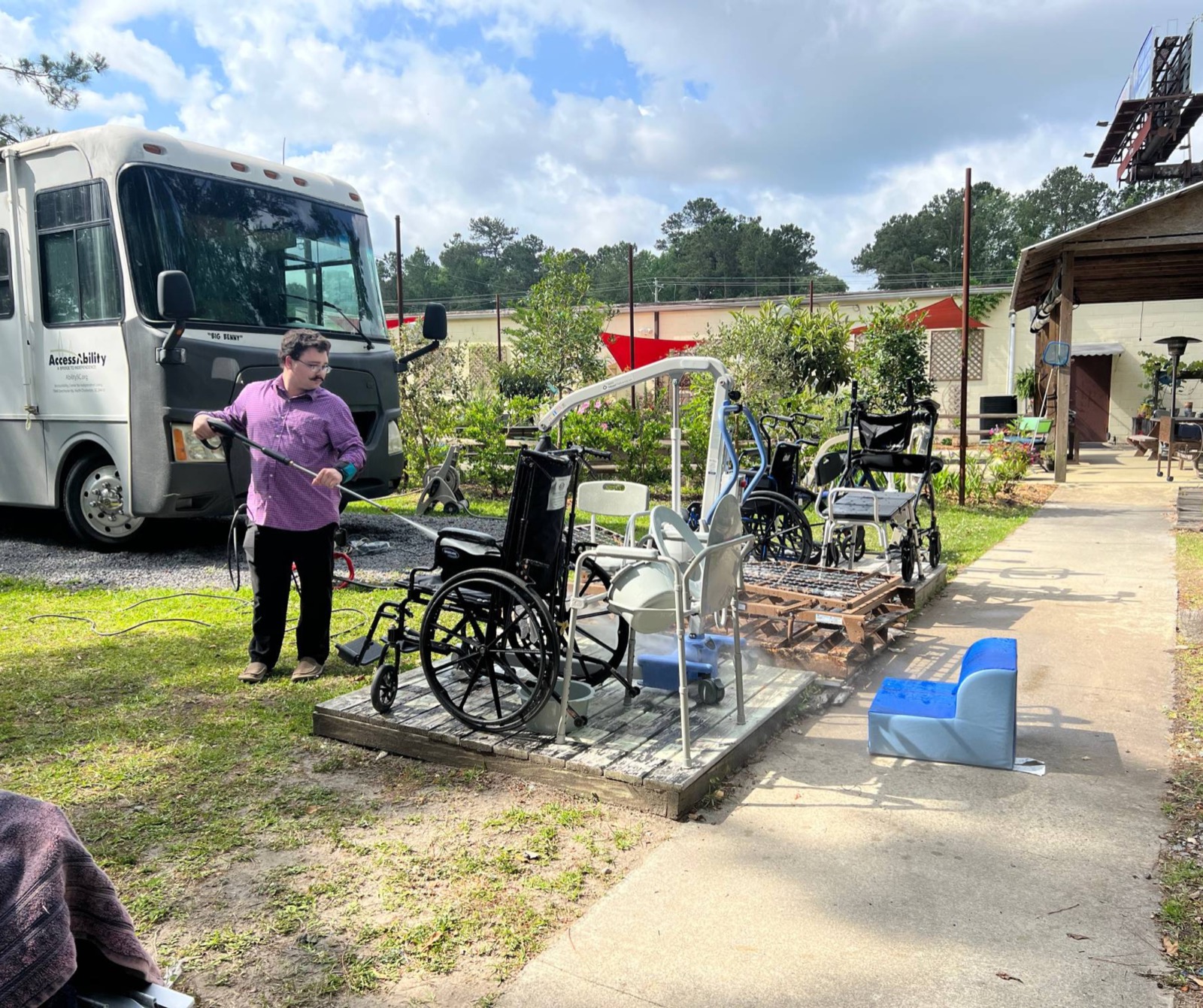An AccessAbility staff member cleaning donated wheelchairs and a Hoyer lift beside the branded mobile unit.